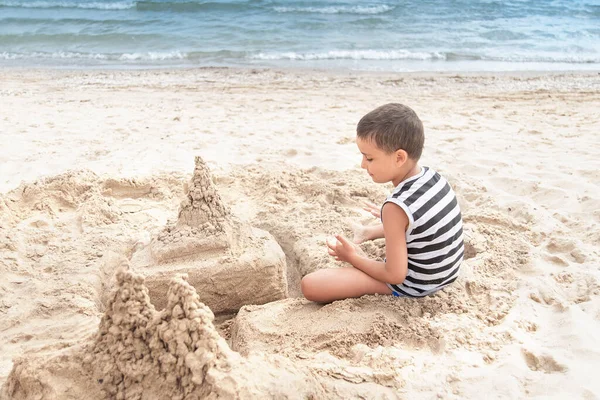 Child builds sand Castle by sea. little kid on beach playing with sand. Boy has fun at vacation.