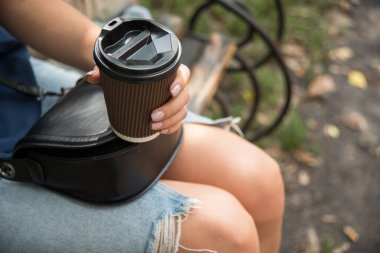 Kahveli kız tahta bir bankta oturuyor. Elinde bir fincan kahveyle tanınmayan genç bir kadın.