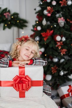 Mutlu heyecanlı kız çocuğu Noel hediyesi kutusunu tutuyor. Süslü odada Noel hediyesi veren bir çocuk. Noel ve insanlar konsepti. Yeni yılınız kutlu olsun. çocuk şimdiki halinden memnun.