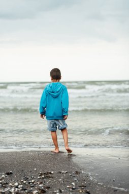 Sad alone kid standing on beach, looking at sea and thinking. The end of summer. sadness about end of vacation