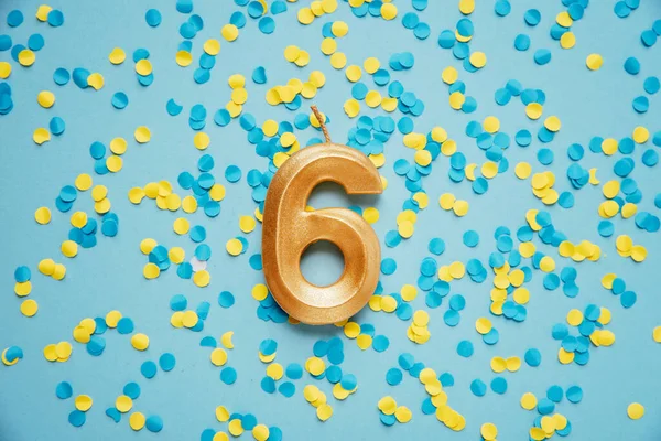 Number 6 six golden celebration birthday candle on yellow and blue confetti Background. Six years birthday. concept of celebrating birthday, anniversary, important date, holiday