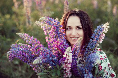 Beautiful young woman holding lupine flowers at sunset on field. concept of nature and romance. Meadow of violet flowers in summer. Enjoying nature and flowers.