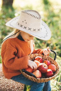 Sonbaharda çiftlikte elma toplayan bir çocuk. Ağaç bahçesinde oynayan küçük kız. Sağlıklı beslenme. Tatlı küçük kız kırmızı lezzetli meyve yiyor. Hasat Konsepti. Elma toplama.