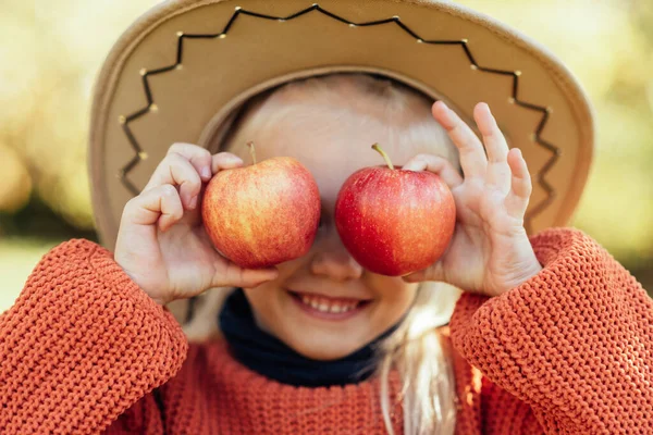 Child picking apples on farm in autumn. Little girl playing in tree orchard. Healthy nutrition. Cute little girl eating red delicious fruit. Harvest Concept. Apple picking.