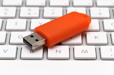 Beyaz klavyeye yerleştirilmiş turuncu USB kalem sürücüsü. Bellek