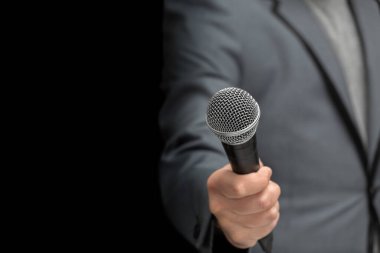 Elinde mikrofon olan bir muhabir ya da muhabir, izole edilmiş siyah bir arka planda. Yakın plan görüntüde mikro