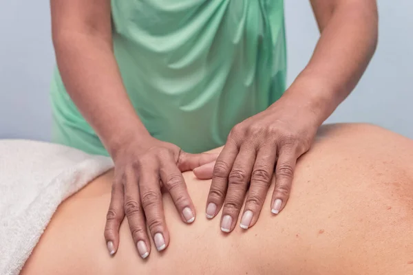 A brown, African-American woman gives a relaxing massage to a Caucasian man. Grey environment