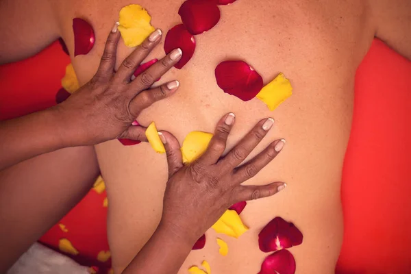 A brunette woman gives a relaxing massage to a Caucasian man. Environment full of rose petals