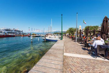 CISANO, İtalya - 26 Mayıs 2021: Cisano di Bardolino adlı küçük bir köyün limanı. Birçok turistin olduğu açık hava restoranları. Garda Gölü. Verona ili, Veneto, İtalya, Avrupa.