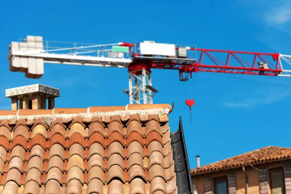 红色和白色的塔式起重机和一个屋顶的特写镜头与梯形瓷砖 意大利语中的Coppo 和排水沟在建筑工地的蓝天上 建筑业概念 意大利 — 图库照片