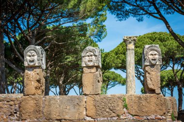 Ostia Antica. Üç tiyatro maskesi ve bir köşe yazısı, antik Roma amfitiyatrosunun dekorasyonu. Roma, İtalya, UNESCO dünya mirası bölgesi. Roma kolonisi M.Ö. 7. yüzyılda kuruldu, Lazio, Avrupa.