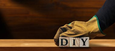 Koruyucu iş eldivenleri olan, ahşap bloklardan yapılmış DIY (Kendin Yap) metnini elinde tutan, boş ahşap tezgahın üzerinde, kopyalama alanı olan.