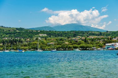 Garda Gölü kıyısında (Lago di Garda) küçük bir köy olan Bardolino 'nun önünde demirli yelkenli teknelerle. Verona, Veneto, İtalya, Avrupa. Monte Baldo 'nun tepelerinde ve sıradağlarında.