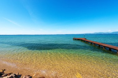 Lazise, Bardolino ve Cisano köylerinin yakınlarındaki Garda Gölü (Lago di Garda) panoramik manzarası ve küçük ahşap iskele. Verona ilindeki turizm beldesi, Veneto, İtalya, güney Avrupa.