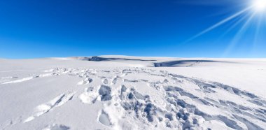 Açık mavi gökyüzü ve güneş ışınlarına karşı toz kar ve ayak izleriyle güzel bir kış manzarası. Lessinia Plateau Bölgesel Doğal Parkı (Altopiano della Lessinia), Verona ili, Veneto, İtalya.