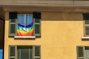 Rainbow flag with text peace in Italian language (Pace), hanging outside a window of a house in an Italian city. Italy, Europe.