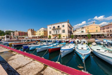 BARDOLINO, İTALYA - 26 Mayıs 2021: Bardolino köyünün küçük limanı çok sayıda gemi demirli. Garda Gölü kıyısındaki turizm beldesi (Lago di Garda). Verona ili, Veneto, İtalya, Avrupa.