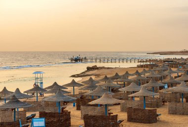 Sabah Marsa Alam yakınlarındaki boş kumlu sahil. Dalış, şnorkelle yüzme ve bir grup plaj şemsiyesi için kullanılan mercan resifinin üzerinde ahşap bir iskele var. Mısır, Afrika.