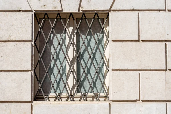 Closeup of a window with wrought iron security bars on a white marble wall. Trentino Alto Adige, Italy, Europe.