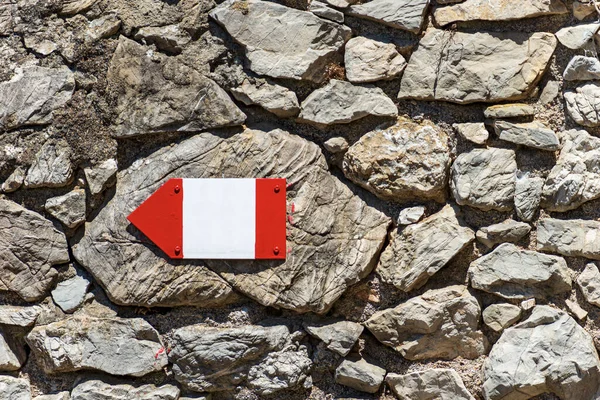 Close-up of a red and white directional trail sign with copy space on a stone wall, footpath in Liguria, Cinque Terre, Italy, Europe.