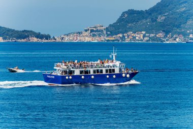 LA SPEZIA, ITALY - JULY 14, 2022: Blue ferry to the Cinque Terre, crowded with tourists in motion in the Gulf of La Spezia in front of the Porto Venere or Portovenere town, Liguria, Italy, Europe.