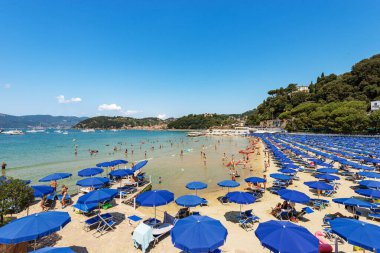 LERICI, ITALY - JULY 16, 2022: Beach of Lerici Town with many umbrellas, tourist resort on the coast of the Gulf of La Spezia, Liguria, Italy, Europe. On background the small village of San Terenzo.