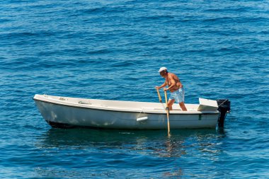 TELLARO, ITALY - JULY 14, 2022: Elderly man rowing on motorboat to dock in the port of the small village of Tellaro, on a sunny summer day, Mediterranean Sea, Gulf of La Spezia, Liguria, Italy, Europe