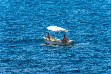 LA SPEZIA, ITALY - JULY 10, 2022:  Small white motor boat with two people on board in motion on a sunny summer day in the blue Mediterranean sea, Gulf of La Spezia, Liguria, Italy, southern Europe. 