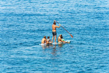 TELLARO, ITALY - JULY 15, 2022: a group of people, an adult male and four children on stand up paddle board or paddleboarding (SUP) in the Mediterranean sea. Tellaro, Gulf of La Spezia, Liguria, Italy.