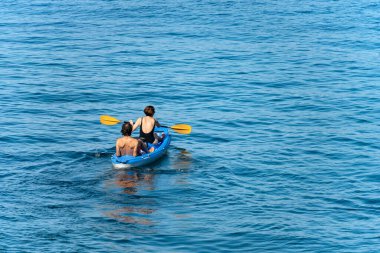 TELLARO, ITALY - July 19, 2022: A mature couple aboard a blue kayak, paddling in the blue Mediterranean sea, on a sunny summer day. Gulf of La Spezia, Liguria, Italy, southern Europe.
