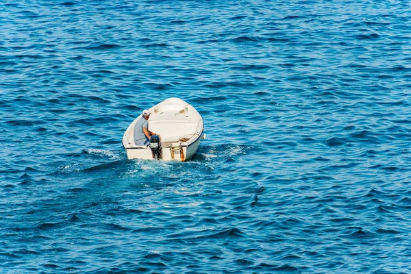 Small white motor boat with one adult man on board runs fast in the blue Mediterranean sea on a sunny summer day, back view. Gulf of La Spezia, Liguria, Italy, southern Europe