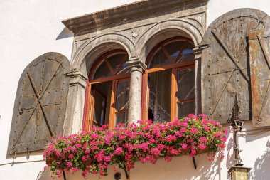 Close-up of an ancient mullion window with metal shutters and geranium flowers. Small village of Malborghetto Valbruna, Val Canale, Udine province, Friuli-Venezia Giulia, Italy, Europe.