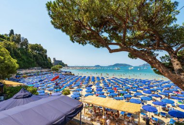 LERICI, ITALY - JULY 16, 2022: Lerici beach with many umbrellas, tourist resort on the coast of the Gulf of La Spezia, Liguria, Italy, Europe. Islands of Tino, Tinetto and Palmaria, Porto Venere town.