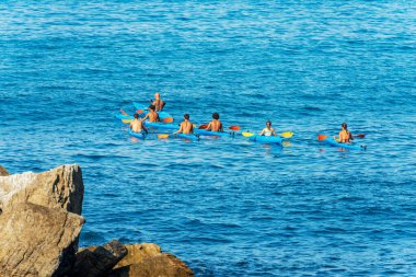 TELLARO, ITALY - JULY 28, 2022: Large group of kayakers in the blue Mediterranean Sea, on a sunny summer day. Tellaro village, Gulf of La Spezia, Liguria, Italy, southern Europe.