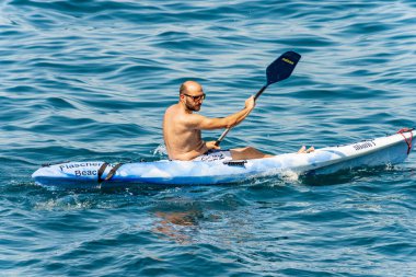LA SPEZIA, İtalya 21 Temmuz 2019: 40-45 yaşlarında yetişkin bir adam güneşli bir yaz gününde mavi bir kanoyla mavi Akdeniz 'de kürek çekiyor. Tellaro köyü, Lerici, La Spezia Körfezi, Liguria, İtalya, Avrupa.