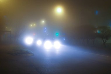 Arabalar sisli havada gece yol alır. Arabanın farları sisi aydınlatıyor.
