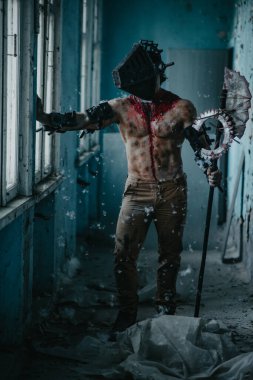 Karanlık odada elinde testere ve baltayla maskeli zombi canavarı görüntüsü olan kanlı bir adam. Cadılar Bayramı konsepti.
