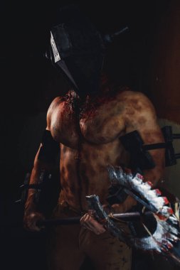 Karanlıkta elinde testere ve baltayla maskeli zombi canavarı görüntüsü olan kanlı bir adam. Cadılar Bayramı konsepti.