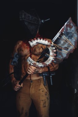 Karanlıkta elinde testere ve baltayla maskeli zombi canavarı görüntüsü olan kanlı bir adam. Cadılar Bayramı konsepti.