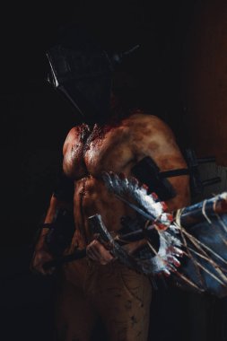 Karanlıkta elinde testere ve baltayla maskeli zombi canavarı görüntüsü olan kanlı bir adam. Cadılar Bayramı konsepti.