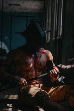 Kafasında maske olan zombi canavarın görüntüsü olan kanlı adam testereyle karanlık odada oturuyor. Cadılar Bayramı konsepti.