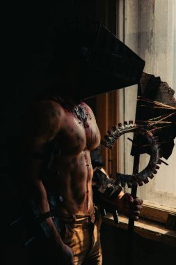 Karanlık odada elinde testere ve baltayla maskeli zombi canavarı görüntüsü olan kanlı bir adam. Cadılar Bayramı konsepti.