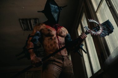 Karanlık odada elinde testere ve baltayla maskeli zombi canavarı görüntüsü olan kanlı bir adam. Cadılar Bayramı konsepti.