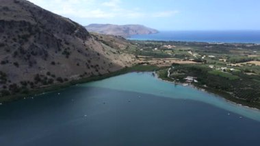 Kournas Gölü 'ndeki İHA' dan güzel bir manzara, su, köy, dağ ve deniz üzerinde yüzen katamaranlar Yunanistan 'ın Girit adasında uzak mesafede..