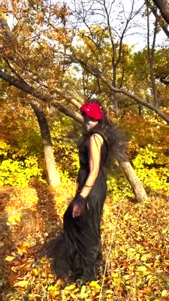 在秋天的森林背景下 一个身穿黑色死亡装束的年轻女子身穿红玫瑰头饰 头戴糖衣走路的垂直画面 死亡日或万圣节的概念 — 图库视频影像