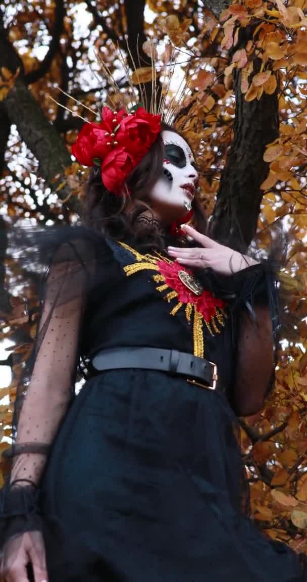 在秋天的森林背景下 一个身穿黑色死亡服装的年轻女子打扮成圣诞老人 头戴糖衣 头戴红玫瑰的垂直画面 死亡日或万圣节的概念 — 图库视频影像