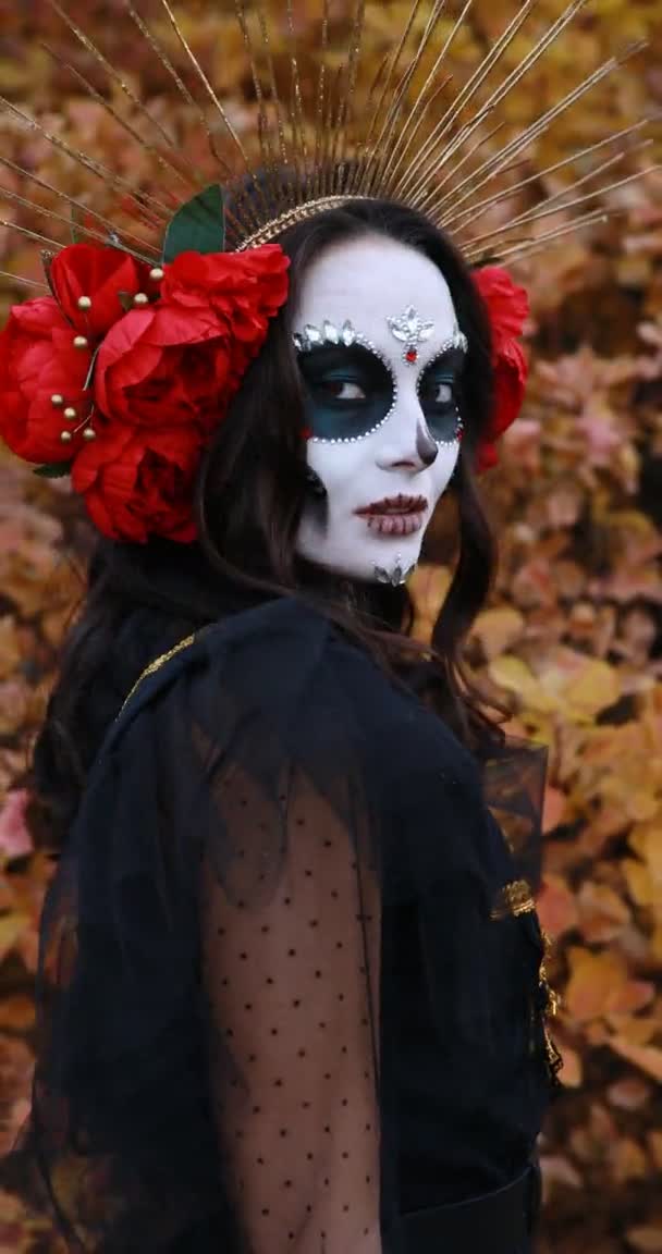 砂糖の頭蓋骨のメイクと死の黒の衣装に身を包んだ赤いバラを持つ若い女性の垂直肖像画サンタ ムエルテ 死者やハロウィーンのコンセプトの日 — ストック動画