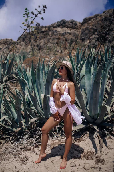 若い女性が帽子 サングラス シャツ 水着で砂漠の中に立っています — ストック写真
