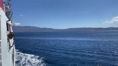 Denizde hareket eden gemiden, deniz köpüğünden ve gökyüzüne karşı dağlardan görüş..