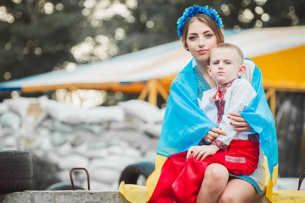 裹着国旗的年轻的乌克兰妇女穿着传统的民族服装坐在路障上 背靠沙袋 俄罗斯对乌克兰军事入侵的概念 乌克兰和欧洲的战争 儿童与战争 — 图库照片